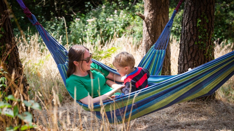 A family relax in hammocks in woodland at Coleton Fishacre, Devon